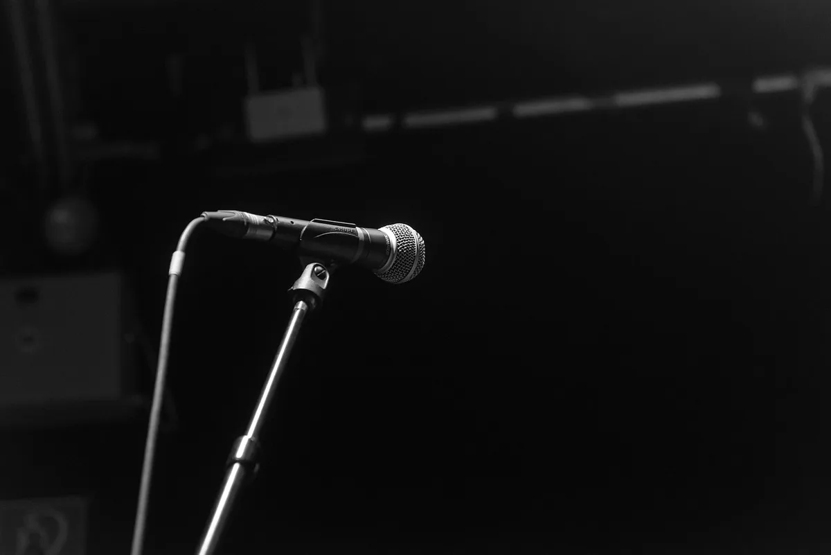 Palco vuoto con microfono e pianoforte in controluce, atmosfera di attesa