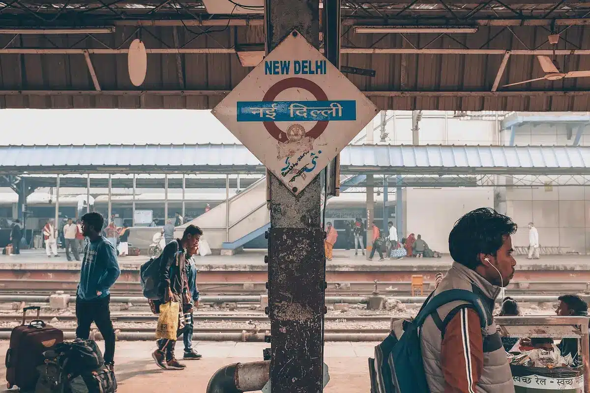 Pendolari anonimi su una banchina ferroviaria con biglietti digitali e tabellone orari sfocato